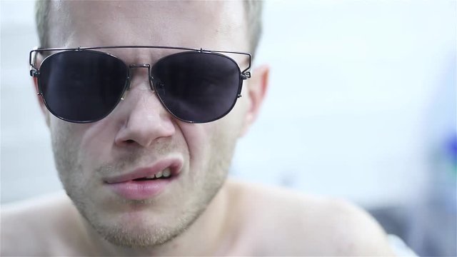 young man in sunglasses impulsively jerks his eyebrows and lip edge. mimic nervous tic.