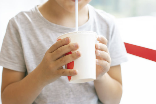 Boy 8 years old drinks milk cocktail from paper cup, fast food concept