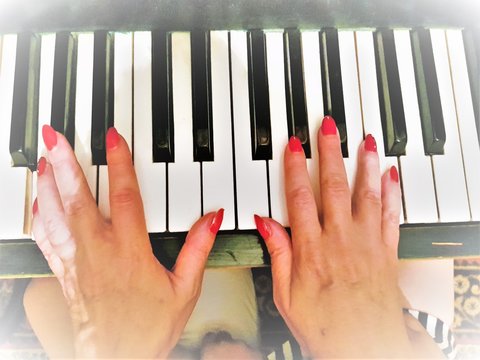 Female hands with a red manicure play the piano