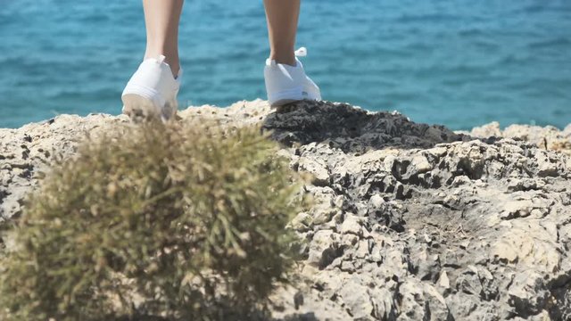 Close-up girl's lags walk on stone cliff at sea. 4K