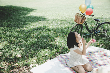 Charming beautiful woman is blowing bubbles to air and they’re flying. Gorgeous beautiful girl sit at park for picnic. Attractive woman has special time, she feel happy with bicycle, grass background