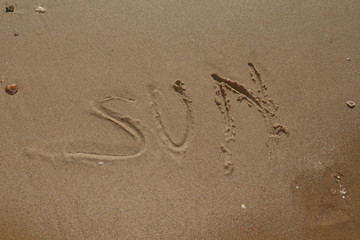 vacation concept with sun word fingered in the sand on the beach