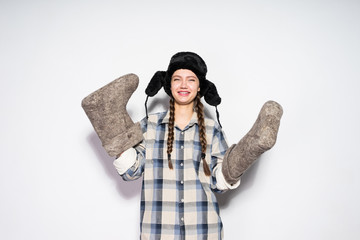 cheerful young Russian girl with pigtails holds gray felt boots, dances and smiles