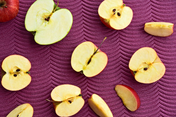 Many sliced red Gala apples on purple background.