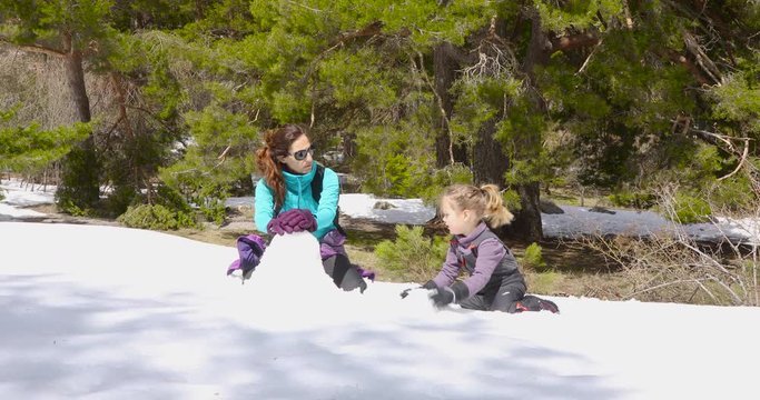 Happy family. Woman mother and four years old blonde child, sitting on their knees, playing with snow to make a sculpture in winter nature. 4k video. 
