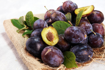 Plums on rustic background. Half of blue plum fruit. Many beautiful plums with leaves