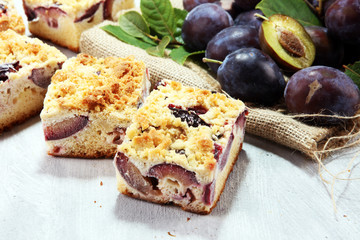 Rustic plum cake on wooden background with plums around.