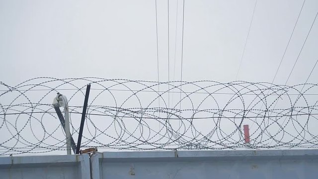 Barbed wire on concrete fence on the background of the grey sky