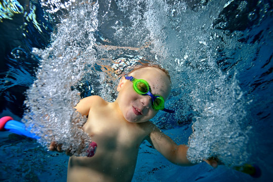 Happy child playing and swimming underwater in the pool with toys in his hands in bubbles. Portrait. Close up. Bottom view. Underwater photography. The horizontal orientation of the image
