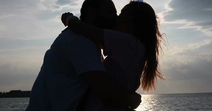 Young romantic couple is enjoying beautiful sunset on the beach and hugging. A woman and a man admiring landscapes. Close up