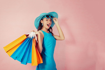 Portrait of a happy Asian pretty girl holding shopping blue bags  away isolated over pink background,colorful shopping concept.