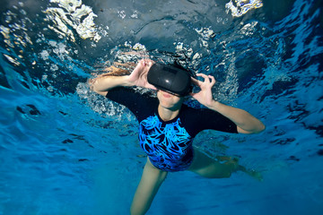 A cheerful girl plays underwater in the pool with black virtual reality glasses on her head. Virtual reality simulator. Shooting underwater. Horizontal orientation