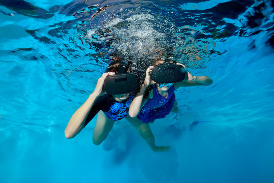Happy baby and mom are swimming and playing with virtual reality glasses on their head underwater in the pool. Shooting underwater. The horizontal orientation of the image