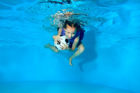 The child swims and dives with a soccer ball underwater in the pool on a blue background. Portrait. Underwater photography. The horizontal orientation of the image