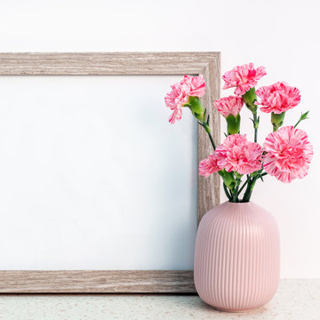 Wooden frame white mockup with a notched vase with pink carnations on a desk with the terrazzo pattern