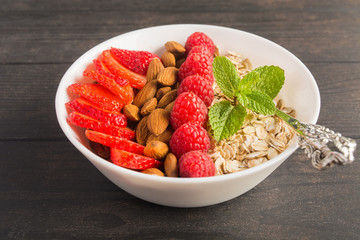 A white bowl with morning breakfast with berries, nuts and mint leaves