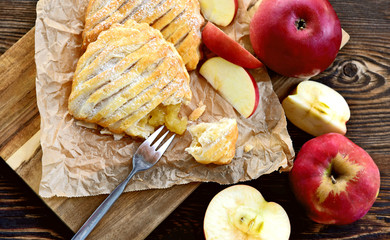 Easy Apple Turnovers (German name is Apfeltaschen) on brown paper with fresh red apples on wooden board and wooden floor.