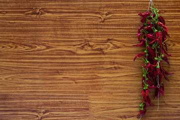 Big bunch of chilli peppers or chili drying on a wooden wall. Organic spices hanging at home with wooden background. Copy space to add text.