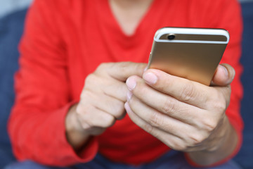 close up hand young male casual wear Red shirt using on cell phone during rest on sofa. sitting in watching message on mobile phone during break relax.