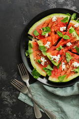 Ripe watermelon roasted on a grill with feta cheese and greens on a concrete background. Appetizing summer snack. Flat lay.