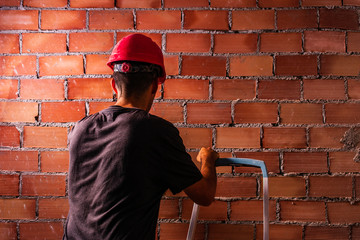 Obrero con casco rojo con escalera delante de un muro de ladrillos