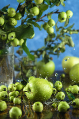 Closeup of green apples and tree branches on wooden table with splashing water, selective focus