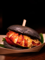 Delicious and tasty Maine Lobster or American lobster Burger with Charcoal Bun under dramatic light. Close up. Such a luxury and gourmet junk food. Close up.