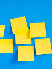 Blank yellow sticky notes on a blue background, concept of business work. Yellow memo stickers on blue wall. Mock-up 