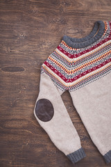 Grey, orange, bordo and beige knitted sweater on wooden background