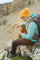 A traveler girl wearing a hat and sunglasses holds a hundred dollar bills in the hands of a fan against the backdrop of cliffs on nature. Keep your head from high cost