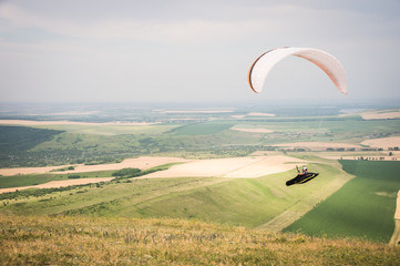 White orange paraglide with a paraglider in a cocoon against the background of fields of the sky...