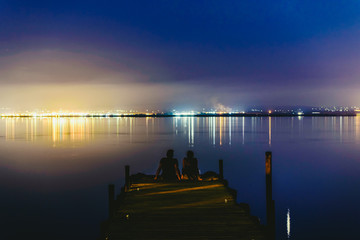 People resting relaxed on a pier on a lake at sunset with calm water