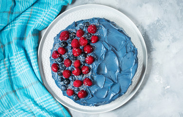 Cake with blue cream and berries on concrete background.