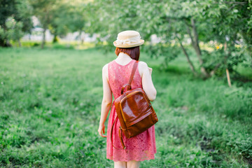 Obraz premium beautiful young woman in the garden. A girl in a straw hat. girl in a crimson dress with a leather backpack