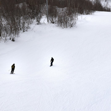 Skier and snowboarder on ski slope at gray winter day