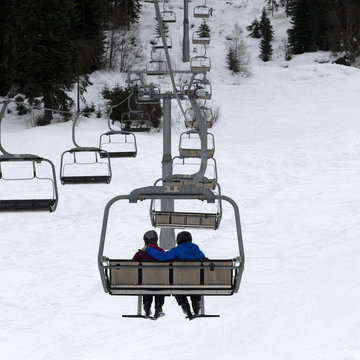 Two skiers on chair-lift in gray day