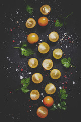 Food background, yellow cherry tomato halves, salt, spices on a dark background, top view and toned image