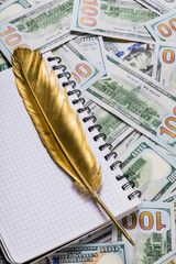 Notebook and Gold quill pen on dollar money background from one hundred dollars