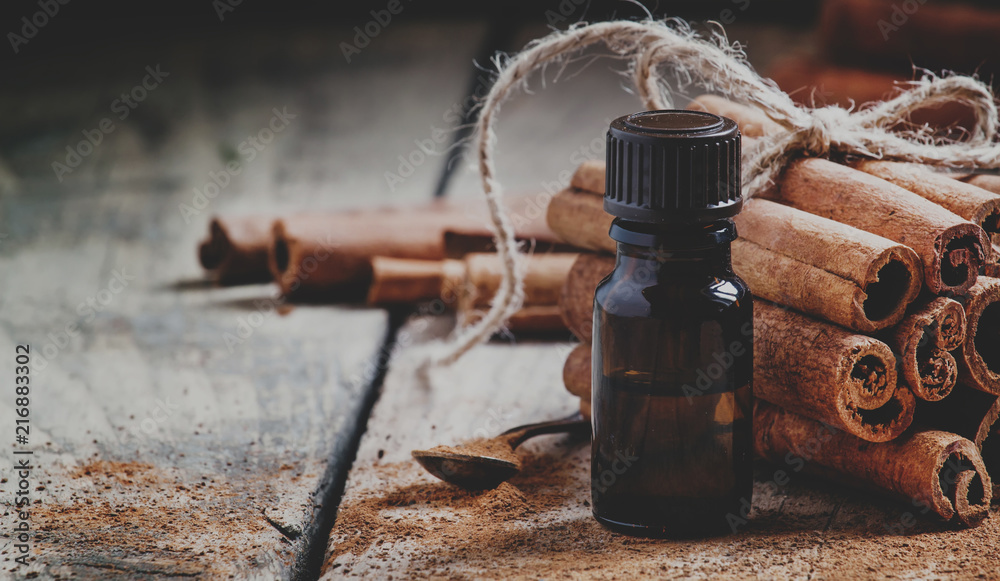 Wall mural essential cinnamon oil in a small bottle, ground cinnamon and cinnamon sticks on old wooden backgrou