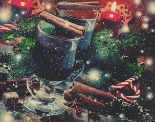 Christmas and New Year mulled wine with cinnamon, cardamom and anise on a background of spruce branches, snowflakes and burning candles, dark toned image, selective focus and toned image