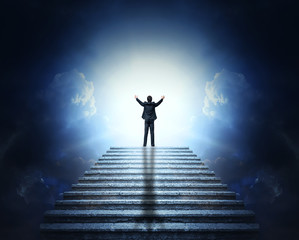 A man in a suit with arms outstretched on a stone staircase to the clouds and light. Stairway to...