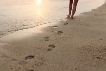 A women walking on the beach at sunset and leaving footprints behind. 