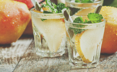 Pear cocktail with soda, fruit slices and mint on an old wooden table, selective focus and toned...