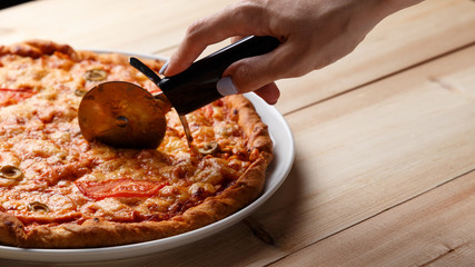 People Hands cutting homemade pizza. Hand slicing a homemade pizza with a cutter on a wooden table