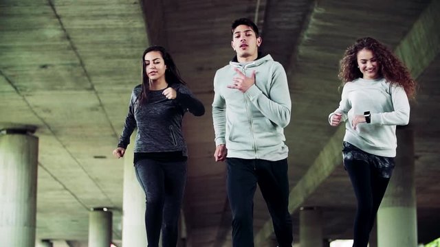 Young athlete friends running under the bridge in the city.