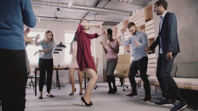 Happy Caucasian woman leader dancing at casual office party. Multiethnic business people celebrate success slow motion.