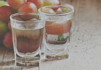 Grappa in a small glass and ripe grapes on old wooden table, selective focus and toned image