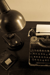 An old typewriter on an old black Desk with a sheet of paper, with a Desk lamp and an ink stamp.