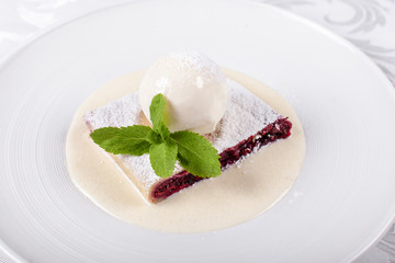 berry strudel cake served with ice cream, mint leaf and vanilla sauce. Classical austrian dessert on white plate. Sweet dessert in the restaurant. Morning light.