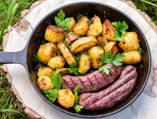 Fried potatoes with meat sausages in a cast-iron frying pan